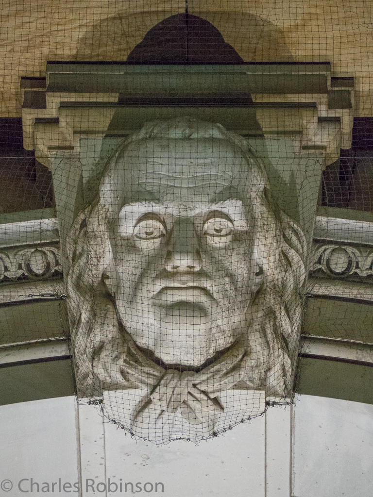 Ben Franklin at City Hall - staring down at us from behind pigeon netting.<br />October 07, 2016@20:42