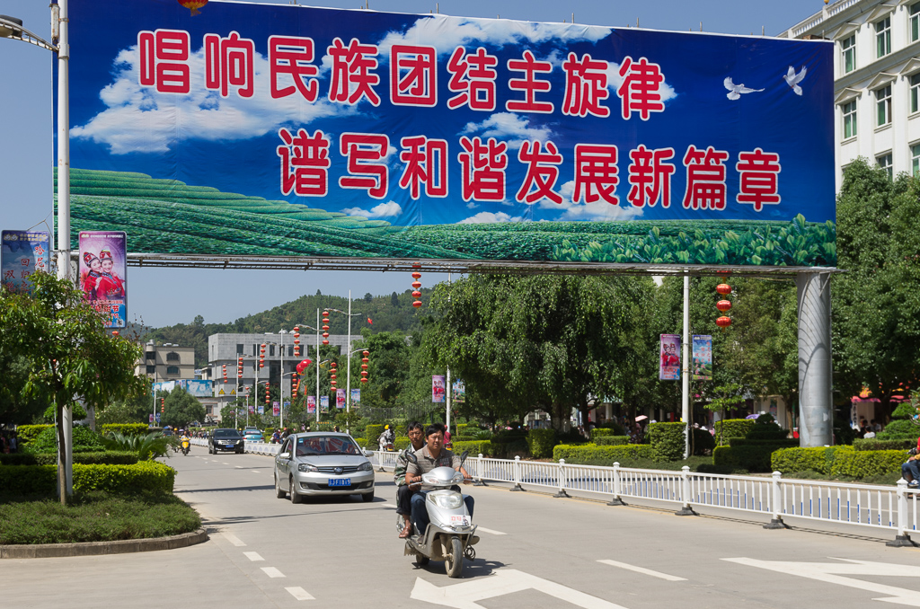 Mojiang main drag near Sun Square.  I took this photo specifically so I could run the billboard through a translator.  Unfortunately my software is not picking out the letters from the clouds very well.<br />May 01, 2015@11:12