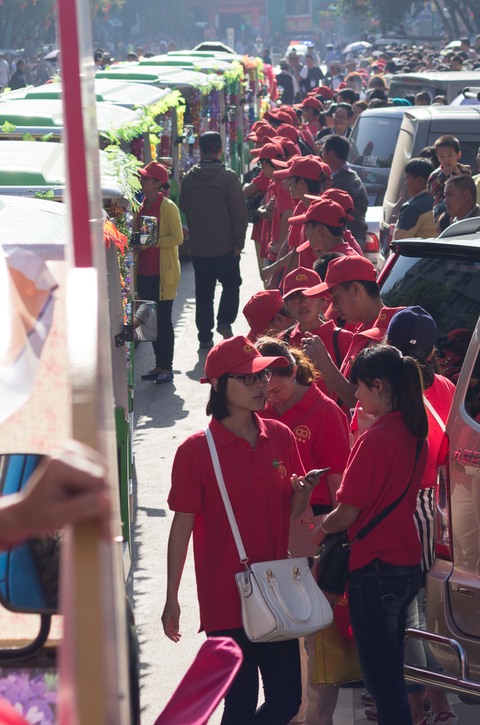 The line of red-shirted guides/volunteers between the floats/cars and the crowds on the sidewalk.<br />May 02, 2015@09:01