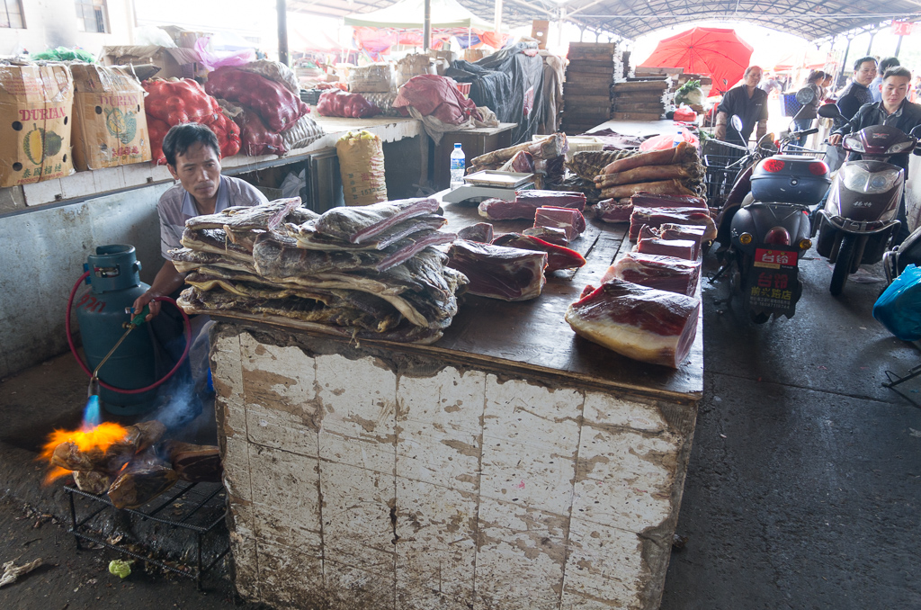 Table full of pork.  The guy behind the counter is burning off the bristles.  Note the scooter making its way down the walkway.<br />April 30, 2015@08:58